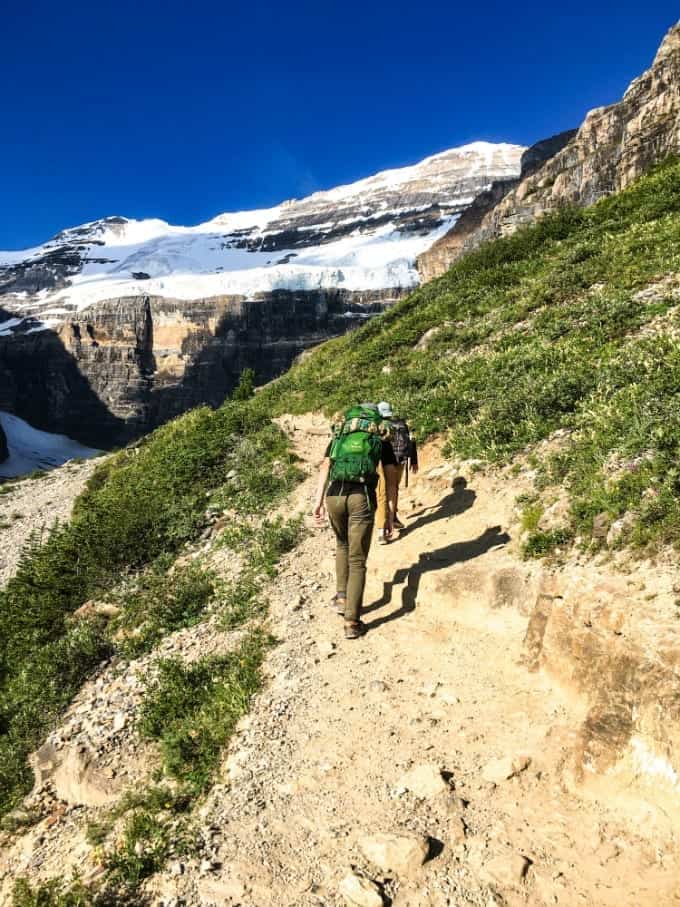 Father and son hiking on trail with snow capped mountains in background.