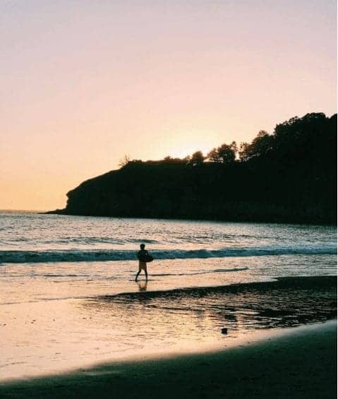 Young boy skim boarding at Muir Beach as sun sets in background