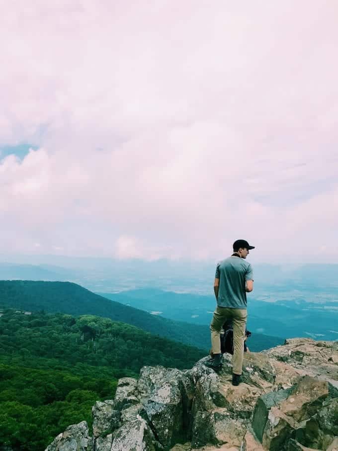 Man standing on top of cliff near hiking trail