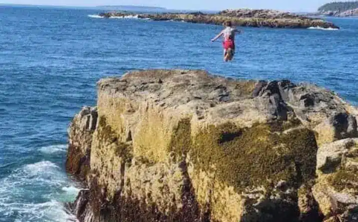 Boy jumping on rocks near ocean in Acadia National Park