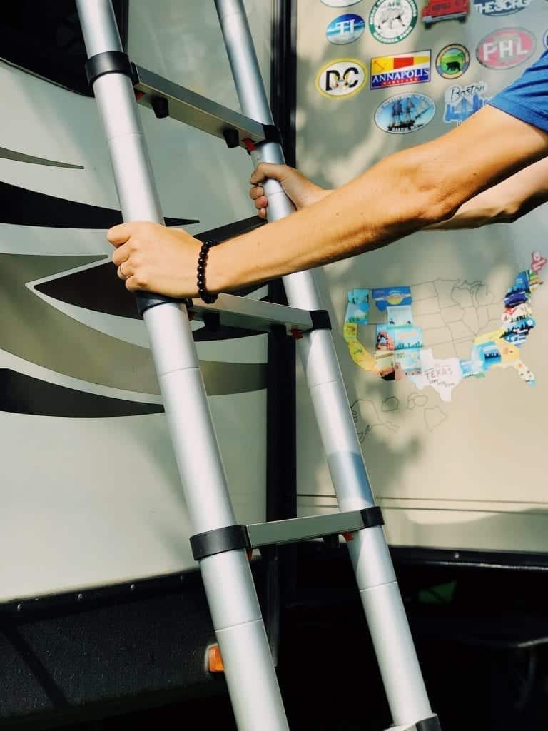 Man's arm placing telescoping ladder against the exterior side of a travel trailer.