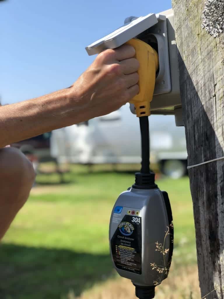 Man's hand pushing surge protector into pedestal power at RV park