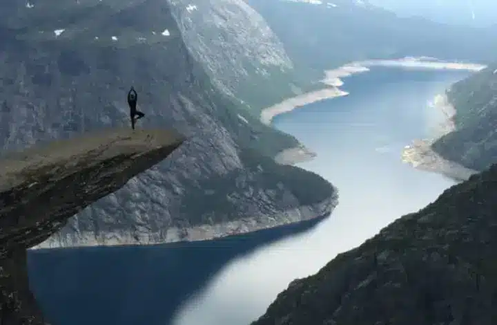 Man in yoga pose on top of cliff overlooking river in Norway