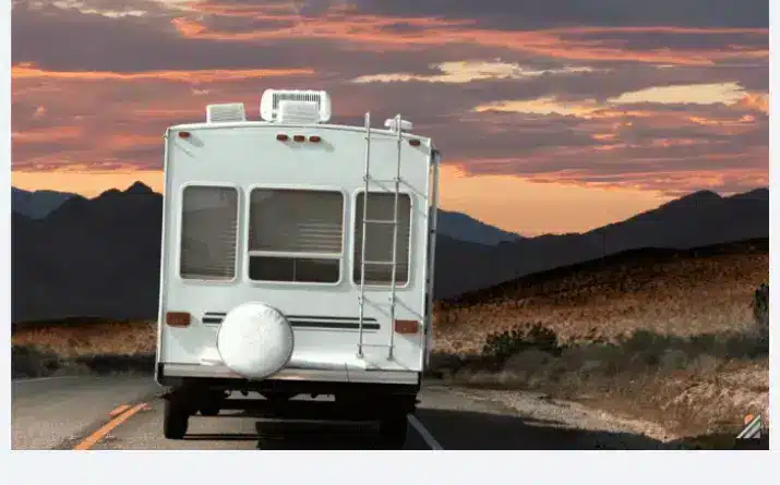 Back of travel trailer that is driving on road toward mountains at sunset.