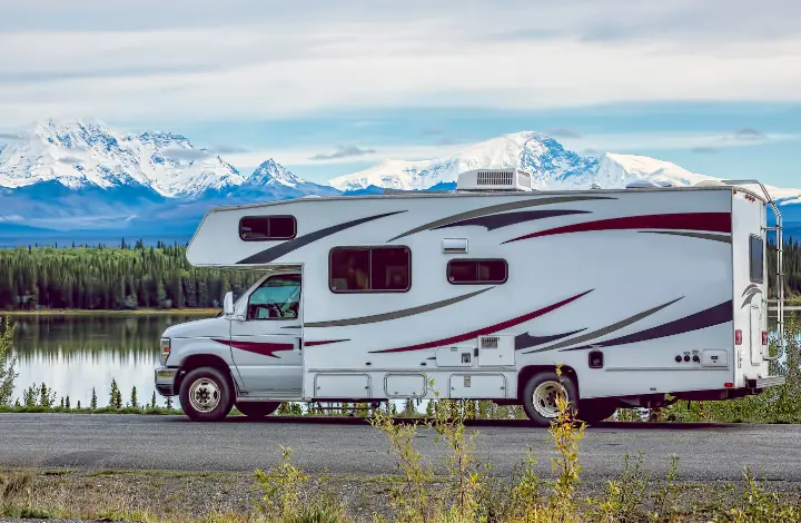 Motorhome driving on road with snow-capped mountains in background inspire desire to rent RV and travel Alaska