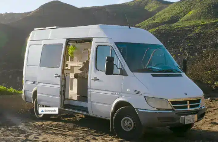 White camper van available for rent in Los Angeles is parked at campsite.