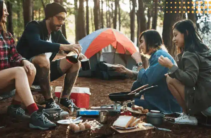 Group of four friends eating a camping breakfast with coffee at campsite