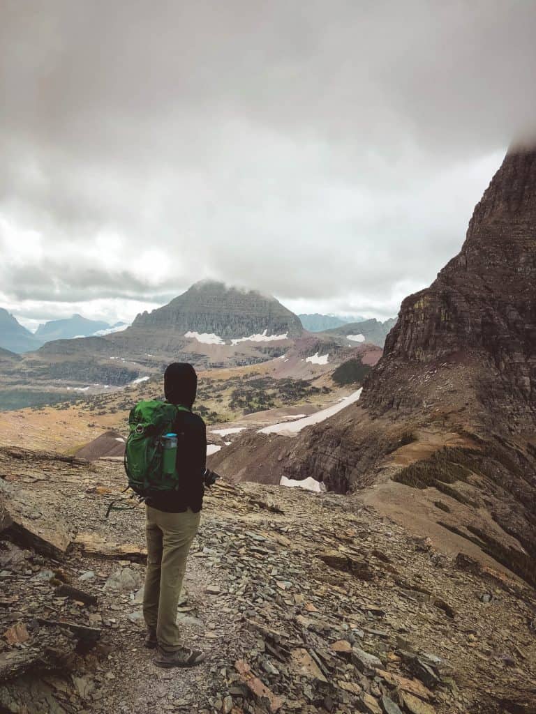 Man in hoodie with back pack on top of cliff while hiking in Glacier National Park