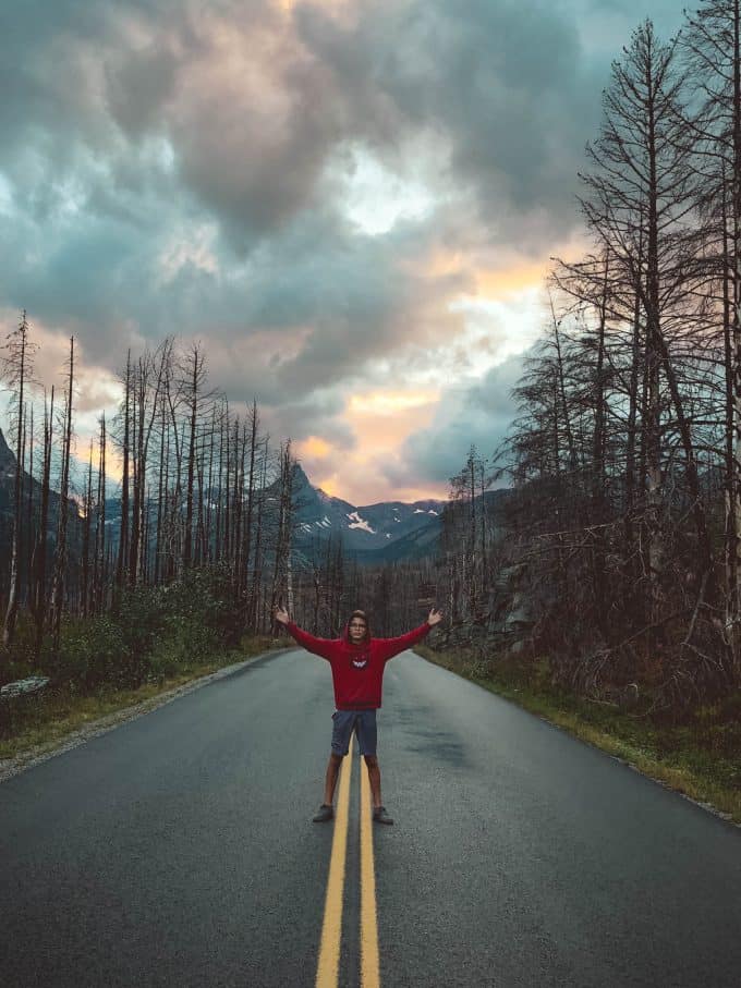 Teenage boy standing in road within Glacier National Park, during fall, the best time to visit the park.