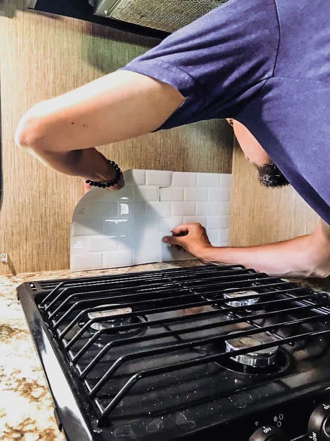 Man installing stick-on tile above stove as part of RV renovation