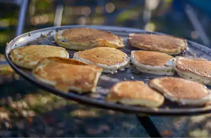 8 round pancakes cooking on griddle over campfire.