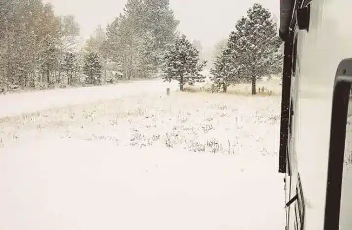 Exterior side of RV with snow falling at campsite during winter RV living