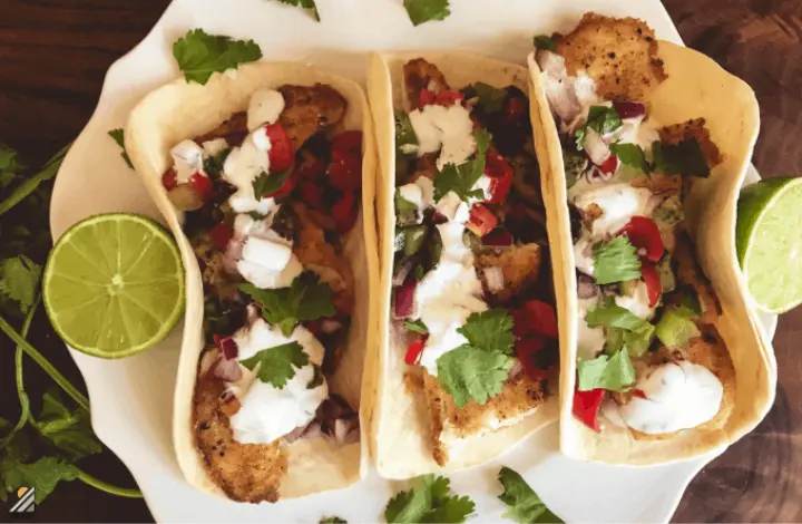 Three fish tacos with salsa on plate with lime.