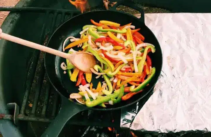 Vegetables cooking in cast iron pan over campfire