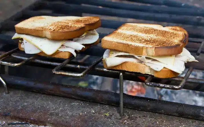 Two sandwiches cooking on the grill over a campfire.