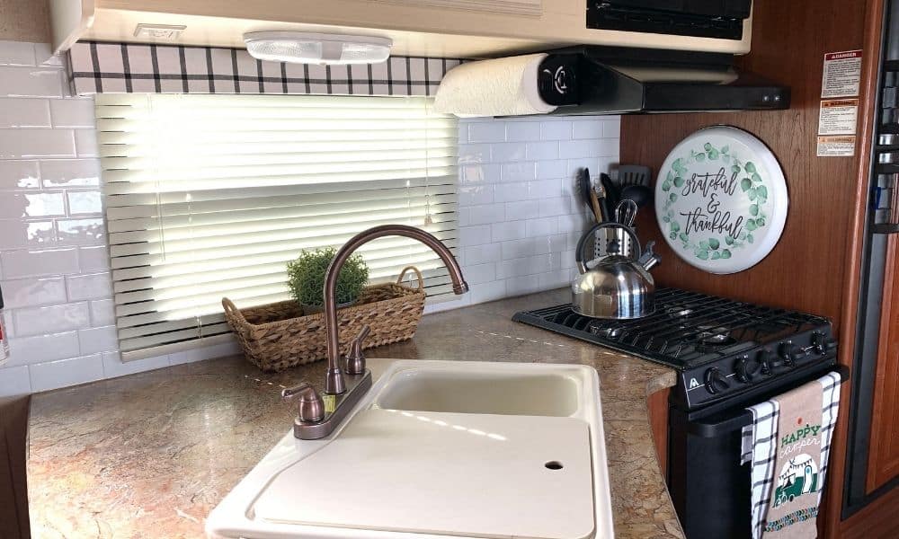 Sink, stove and stick-on white subway tiles on the interior wall of an RV