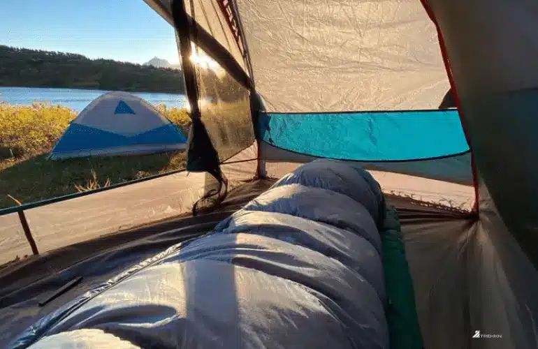 Sleeping bag and pad inside tent at campsite near lake.