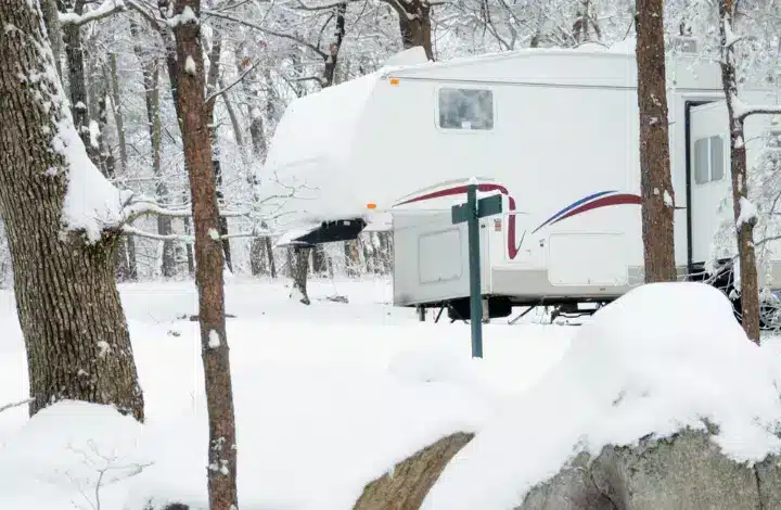 Travel trailer RV parked at campsite in winter with snow covering ground