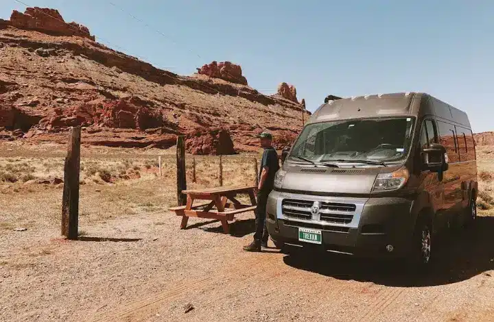 Man leaning on black campervan parked near picnic table