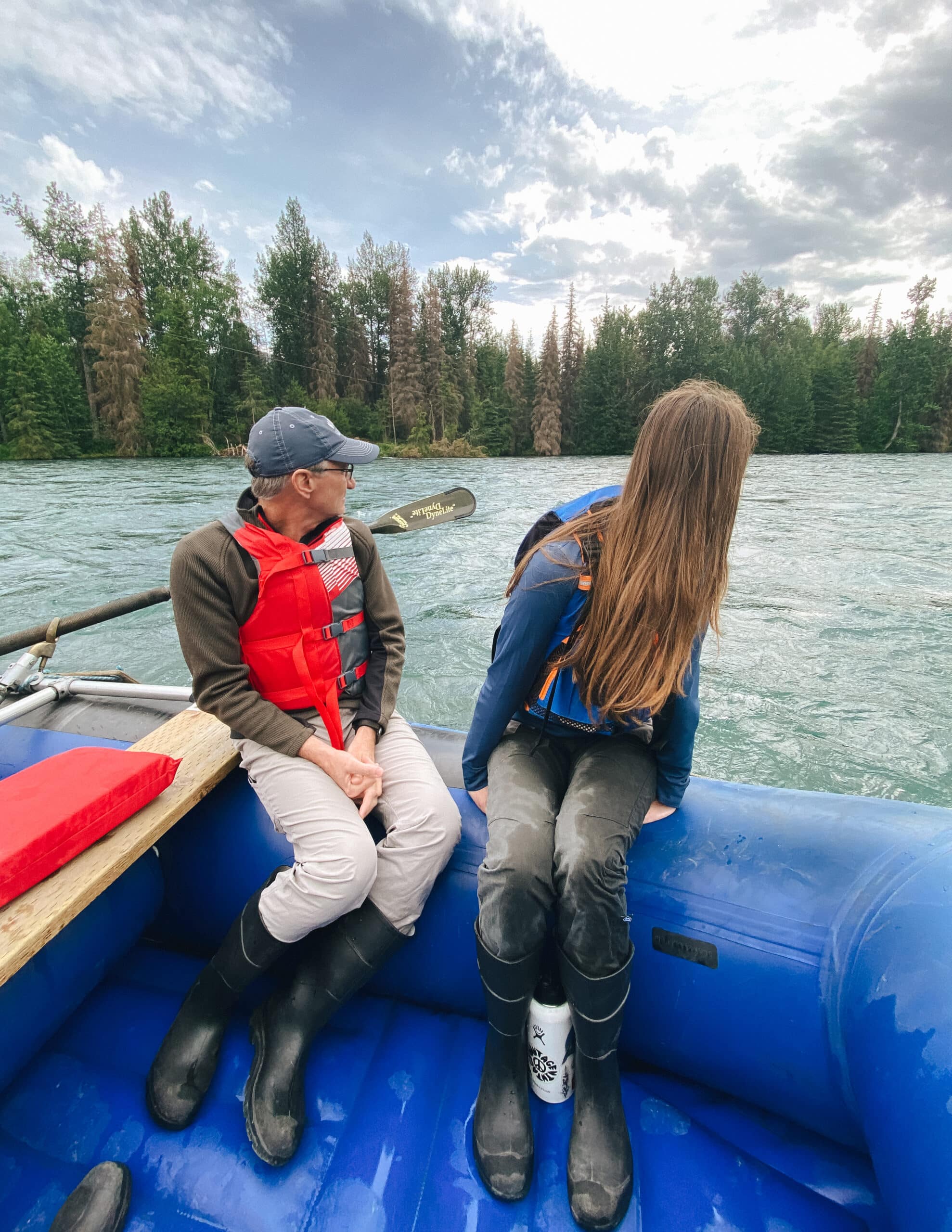 Man and woman in rubber boots sitting on side of river raft