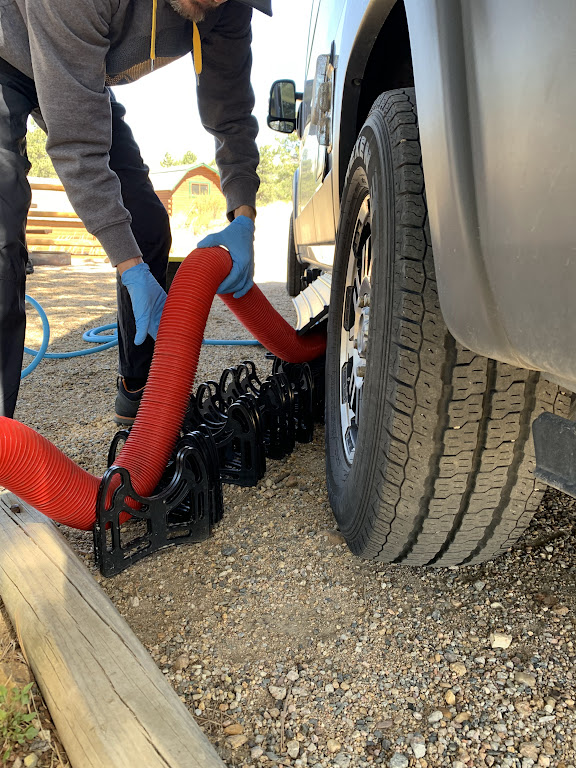 Man setting up RV sewer hose to empty black tank at a campsite.