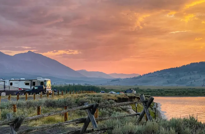 Class A RV and Jeep parked near river at sunset