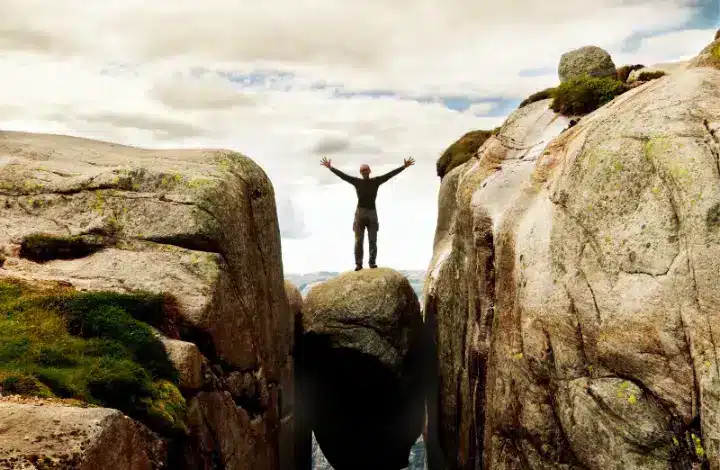 Male hiker standing on top of boulder wedged between two cliffs