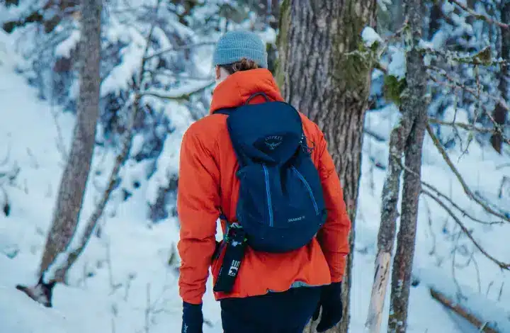 Man wearing red jacket and backpack hiking on snow covered trail