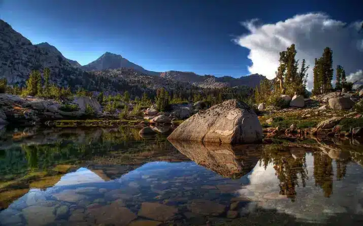 Crystal clear lake near mountains and evergreen trees.