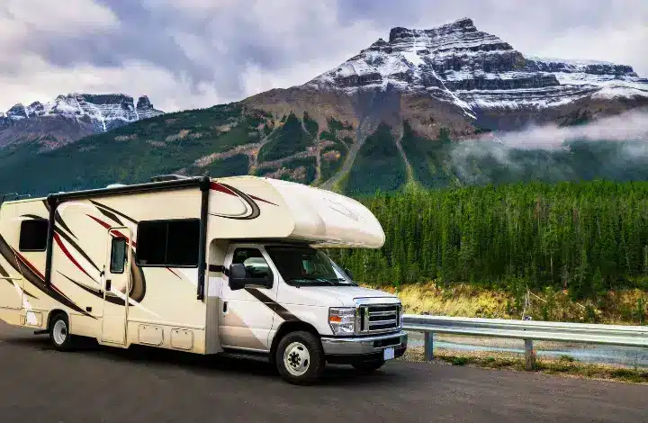 White Class C driving on road with snow capped mountain in background.