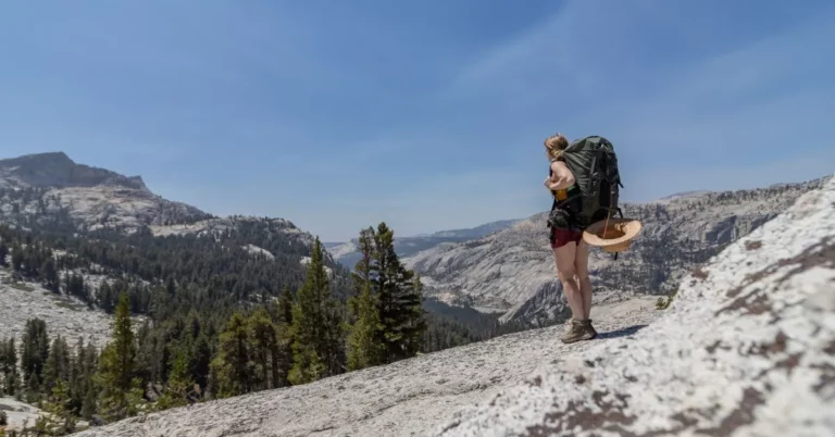 A solo hiker standing on boulder overlooking valley and mountains.