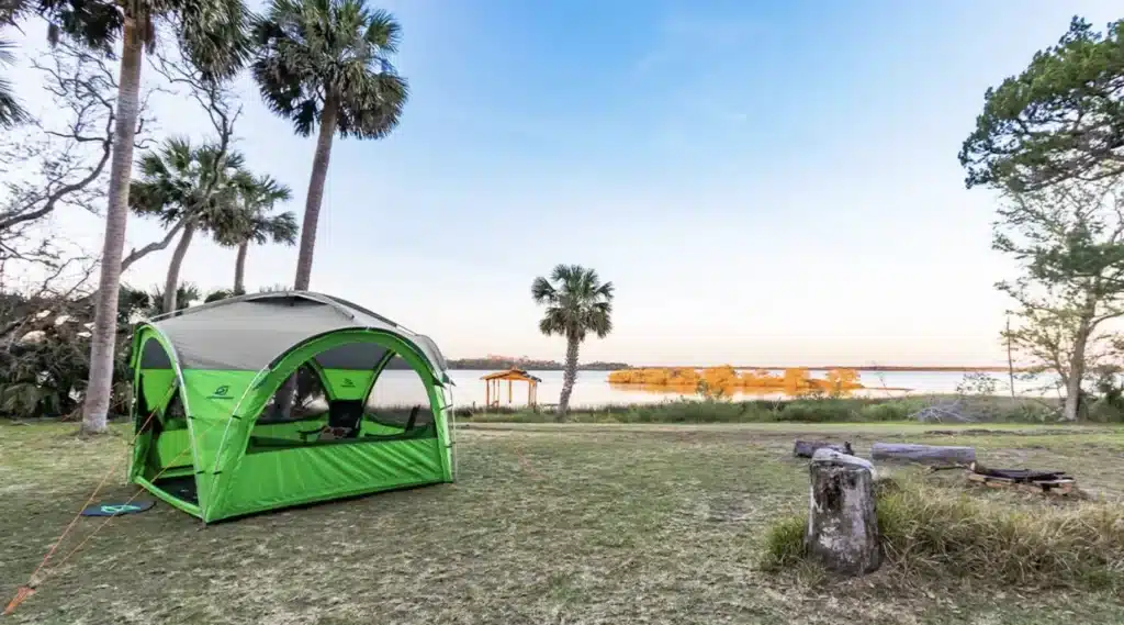 Green GOzeebo brand tent pitched at campsite near lake.