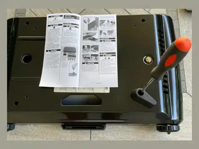 A screwdriver is used to install plastic feet on bottom of small portable grill.