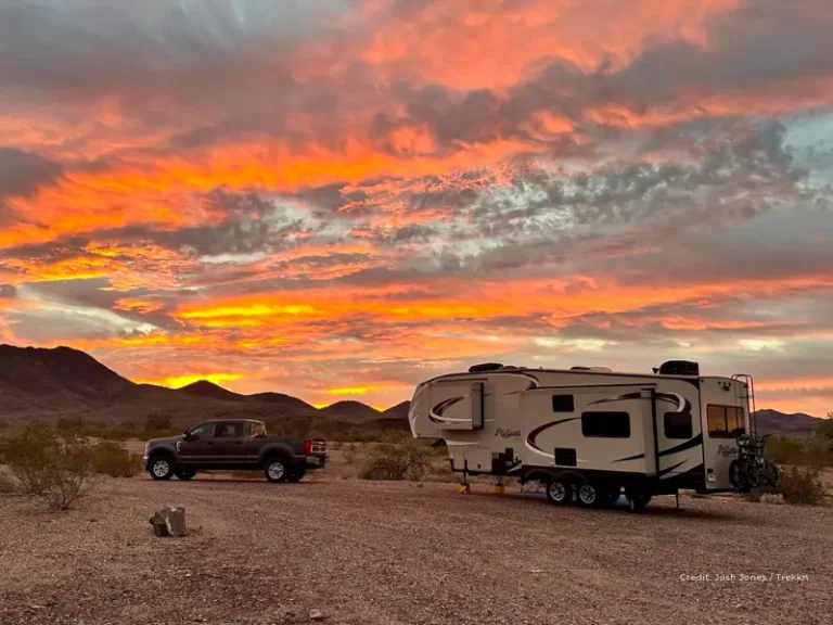 Tow vehicle and fifth wheel RV with orange sunset in background.