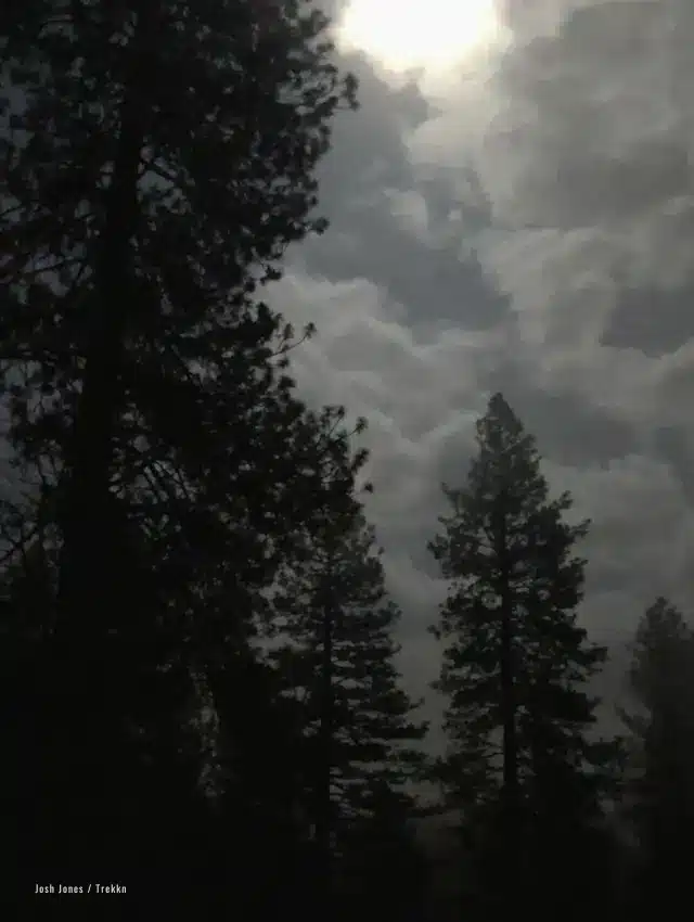 Moon peeking through dark clouds at campsite.